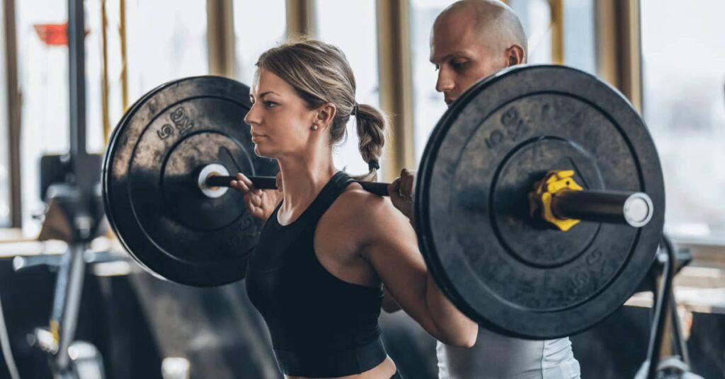 a girl lifting weight and a trainer helping her